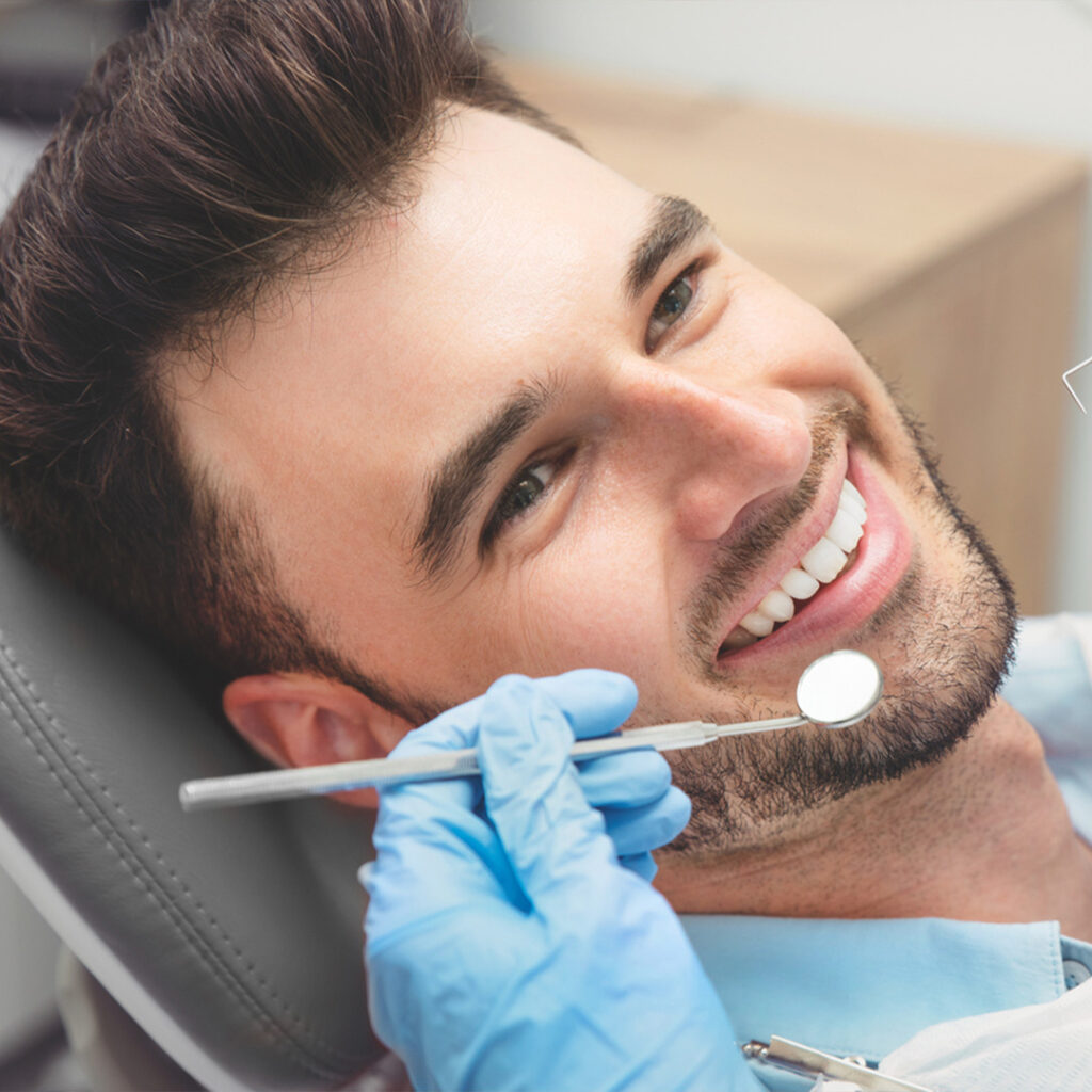 A man lying in a dental chair with a hand near his cheek wearing a blue glove and holding a dental mirror.